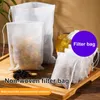 Several non-woven filter bags filled with herbs and tea are displayed on a wooden tray, with a glass of tea in the background. Produktbild-Vorschau