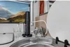 A water filter is shown in use on a kitchen counter in what appears to be an RV or small living space, with a window showing a mountain landscape. Náhled obrázku produktu