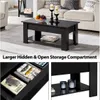 A black coffee table with storage compartments is shown in a living room setting, with a sofa in the background. Produktbild-Vorschau