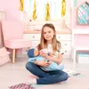 A young girl is sitting on the floor, feeding a baby doll a bottle in a child's bedroom. Produktbild-Vorschau