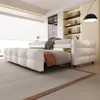 A modern bedroom with a white sofa bed extended into a bed, featuring a plaid blanket and an orange accent pillow. Produktbild-Vorschau