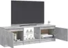 A modern TV stand with a light gray, concrete-like finish, featuring multiple compartments and open shelves. A large flat-screen TV is placed on top, and there are decorative items and books on display inside the shelves. One of the cabinet doors is open,  Produktbild-Vorschau