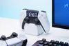 A PlayStation PS5 controller alarm clock is displayed on a white desk next to another controller and a keyboard, with a computer monitor in the background. Náhled obrázku produktu