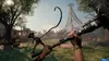 A first-person perspective of a video game scene, showing a character holding a whip-like weapon in a sunny outdoor environment with tents and a large, abstract structure in the background. Produktbild-Vorschau