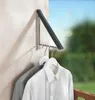 A wall-mounted folding clothes rack with two shirts hanging on it, outdoors with greenery and sky in the background. Produktbild-Vorschau