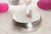A round, hammered metal coffee table with decorative items on top, surrounded by colorful poufs on a wooden floor. Produktbild-Vorschau