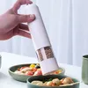 A hand holding a white electric pepper grinder over bowls of food. Podgląd zdjęcia produktu