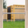 A metal bar attached to wooden posts, with a blurred playground in the background. Produktbild-Vorschau