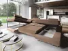 A large, modular sectional sofa with its sleeping and storage features extended, set in a modern living room with large windows overlooking a garden. Podgląd zdjęcia produktu