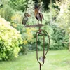 A decorative metal garden stake with two bird figures in a garden setting. Podgląd zdjęcia produktu