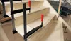 A close-up view of wooden stairs being constructed, with several clamps holding the pieces together. Voir les images du produit