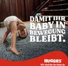 A baby wearing a diaper is doing a handstand on a plush gray carpet in a home setting. Text and a brand logo are overlaid on the image. Produktbild-Vorschau