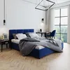 A bedroom with a blue upholstered bed, nightstand, desk, and chair, with a large window overlooking trees. Produktbild-Vorschau