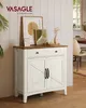 A VASAGLE sideboard with two doors and a drawer, decorated with framed art and a vase of dried flowers, in a room with wooden floors and white paneled walls. Produktbild-Vorschau