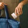A person is putting a small drinking cup into a large blue tote bag. Produktbild-Vorschau