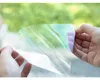 Hands holding a piece of iridescent film with a blurred green background. Náhled obrázku produktu