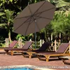 A patio umbrella shades lounge chairs by a pool. Produktbild-Vorschau