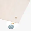 A close-up shot of a piece of beige fabric with several grommets and a grommet setting tool laid out on a white surface. Produktbild-Vorschau