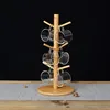 A wooden mug tree with clear glass mugs hanging from it, set against a black background and on a table. Produktbild-Vorschau
