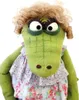 A close-up studio shot of a green alligator puppet wearing a floral dress and a curly blonde wig. Anteprima dell’immagine prodotto