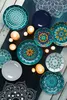 A collection of decorative plates and candles arranged on a dark blue mat with a wooden surface underneath. Podgląd zdjęcia produktu