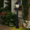 A black lamppost stands in front of a building with ivy and hydrangeas. Produktbild-Vorschau