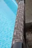 A close-up of a pool ladder rail with a rattan-like texture, next to a blue pool. Produktbild-Vorschau