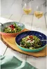 Two decorative bowls filled with food and two glasses of white wine are arranged on a wooden board. Voir les images du produit