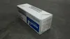 A white cardboard box for a printer toner cartridge sits on a textured gray surface. Voir les images du produit