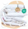 A folded white duvet with beige trim, presented with marketing tags and decorative feathers. Produktbild-Vorschau