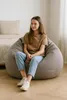 A young girl sits on a large, gray beanbag chair in a bedroom. The bed is visible in the background. Anteprima dell’immagine prodotto