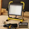 A work light and a cordless drill are displayed on a wooden surface, with some lumber in the background. Produktbild-Vorschau