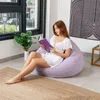 A young woman is sitting on a light purple beanbag chair and reading a book. Anteprima dell’immagine prodotto
