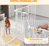A dog is standing next to a white metal pet gate. A close-up inset shows a hand operating the latch mechanism of the gate. Produktbild-Vorschau