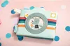 A children's fabric photo album shaped like a camera, decorated with colorful stripes and a cartoon character, placed on a pink surface with confetti. Anteprima dell’immagine prodotto