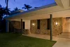 Exterior view of a modern house at dusk, featuring a stone wall with two wall lamps and a covered walkway. Produktbild-Vorschau