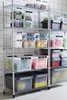 Shelving units filled with various clear and colored storage containers, some containing food items like fruits and vegetables. Produktbild-Vorschau