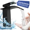 A black waterfall faucet is shown with water flowing into hands covered in soap, with water splashing around the faucet. Produktbild-Vorschau