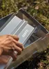 A hand is assembling a metal grill outdoors on grass. Produktbild-Vorschau