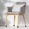A gray fabric chair with wooden legs sits against a light gray wall. A pillow with a white leaf pattern is on the seat of the chair. Small black caps are on the feet of the chair legs. Produktbild-Vorschau