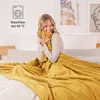 A woman is sitting on a bed, wrapped in a yellow blanket. Voir les images du produit