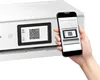 A hand holding a smartphone displaying a QR code, positioned next to a printer that is also displaying a QR code on its screen. Podgląd zdjęcia produktu