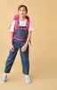 A young girl wearing a backpack and overalls stands against a plain background. Anteprima dell’immagine prodotto