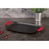 A black griddle pan with red handles rests on a dark, textured countertop. Scattered red petals are visible on the left side of the countertop, and a small potted plant is in the background. Anteprima dell’immagine prodotto