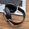 A pair of black and gold headphones rests on a wooden surface next to a laptop. Voir les images du produit