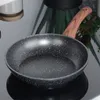 A close-up shot of a black frying pan with a wooden handle, placed on a reflective black surface. Anteprima dell’immagine prodotto