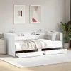 A white daybed with drawers and a shelf headboard, made up with bedding and pillows, is shown in a bedroom setting with artwork on the wall and a plant in the background. Náhled obrázku produktu