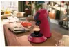 A red coffee maker brewing coffee on a wooden table, with headphones and a laptop in the background. Produktbild-Vorschau