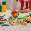 A collection of colorful children's toys scattered on a textured rug, with a red rocking horse in the background. Produktbild-Vorschau