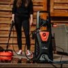 A person is using a pressure washer on a wooden deck. Voir les images du produit